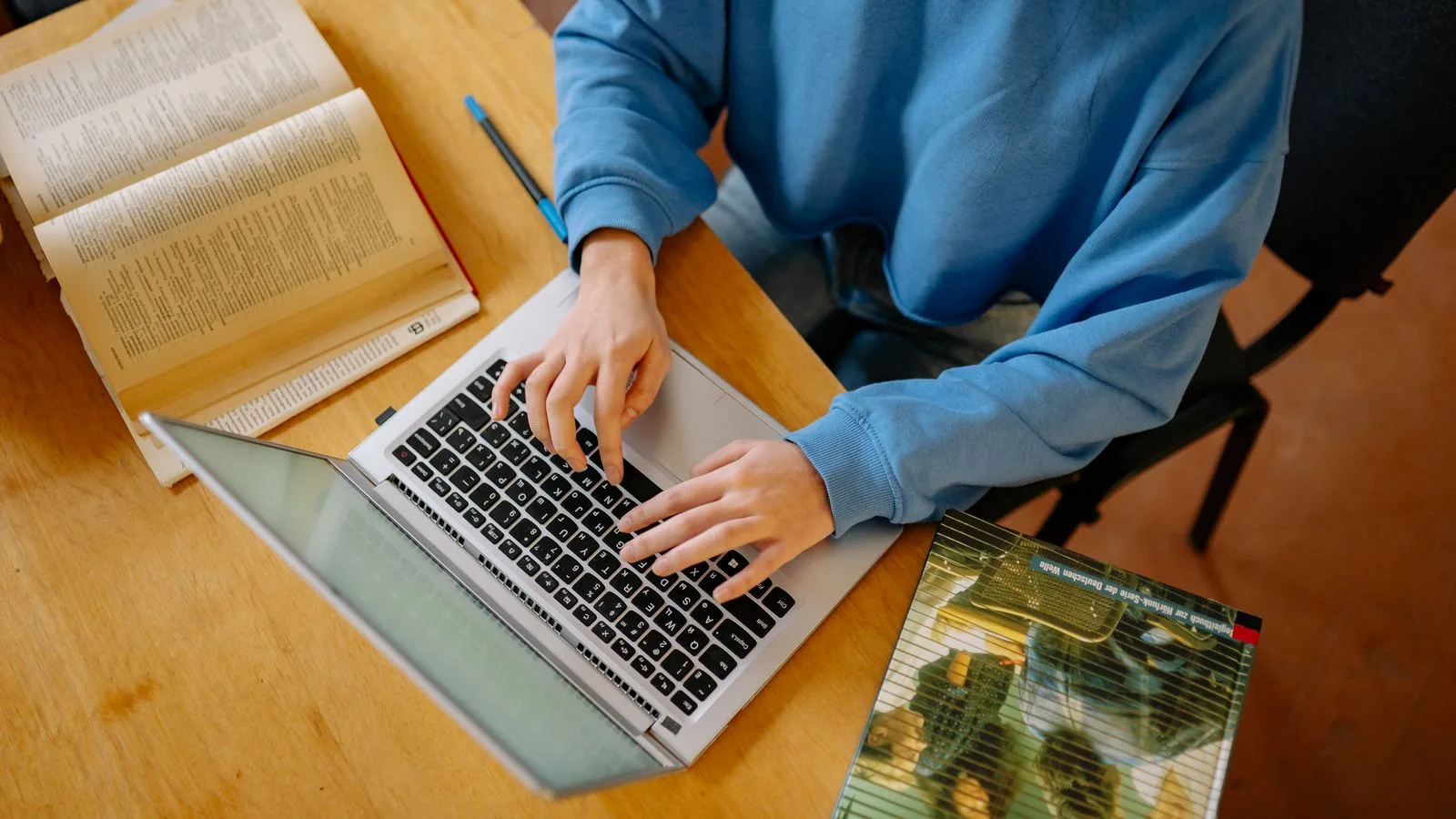 Student checking information on a laptop while comparing open books and research notes